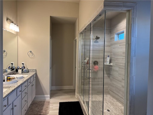 bathroom with a sink, a shower stall, baseboards, and double vanity