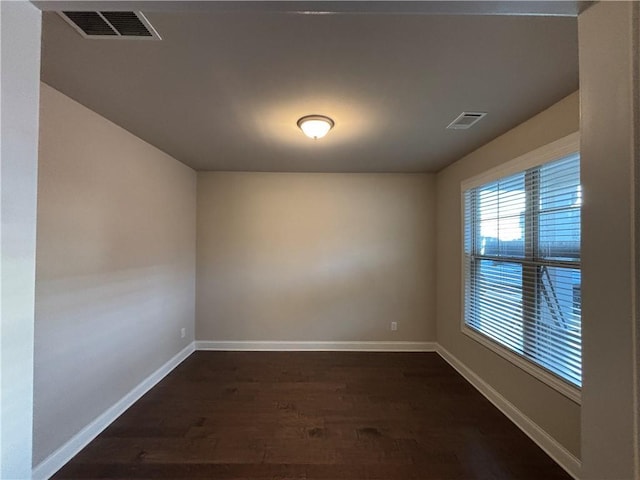 unfurnished room featuring dark wood-style floors, visible vents, and baseboards