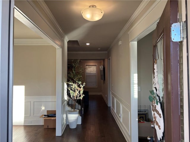 hall with a wainscoted wall, ornamental molding, a decorative wall, and dark wood finished floors