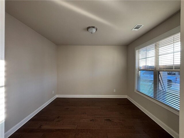 empty room featuring dark wood-style floors, baseboards, and visible vents