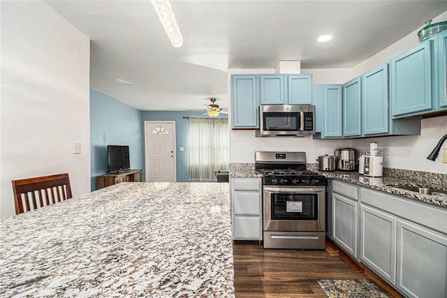 kitchen featuring blue cabinets, a sink, appliances with stainless steel finishes, light stone countertops, and dark wood-style flooring