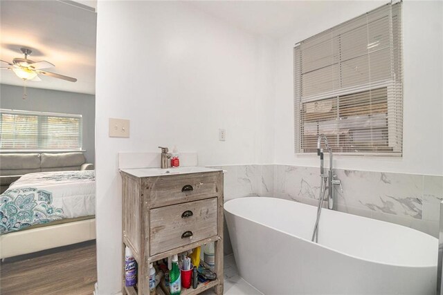 ensuite bathroom with a wainscoted wall, connected bathroom, tile walls, a freestanding bath, and ceiling fan