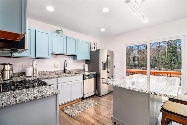 kitchen with light stone countertops, stainless steel appliances, a sink, light wood-style floors, and a kitchen breakfast bar