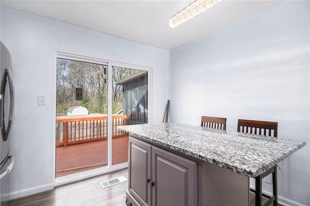 kitchen with visible vents, a breakfast bar, baseboards, and wood finished floors