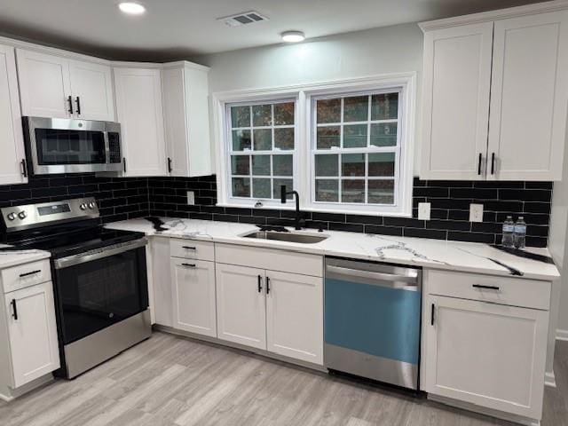 kitchen featuring sink, white cabinetry, stainless steel appliances, and light hardwood / wood-style flooring