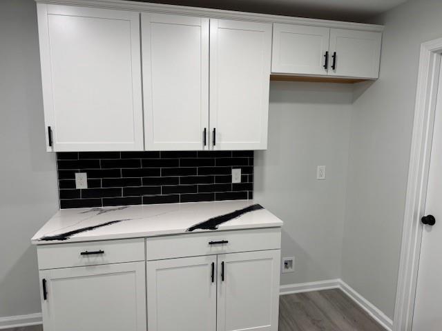 kitchen with backsplash, white cabinetry, light stone counters, and wood-type flooring