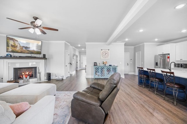 living room featuring beamed ceiling, ceiling fan, crown molding, and light hardwood / wood-style flooring