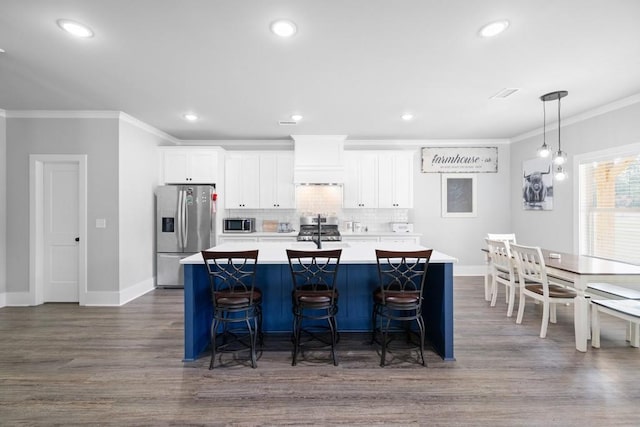 kitchen featuring white cabinets, crown molding, dark hardwood / wood-style floors, appliances with stainless steel finishes, and a kitchen bar