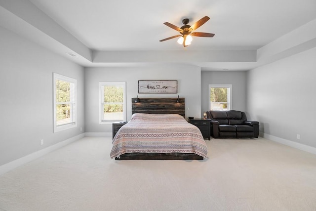 carpeted bedroom with a raised ceiling and ceiling fan