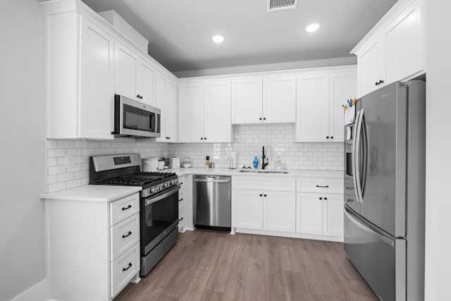 kitchen with sink, stainless steel appliances, light hardwood / wood-style floors, decorative backsplash, and white cabinets