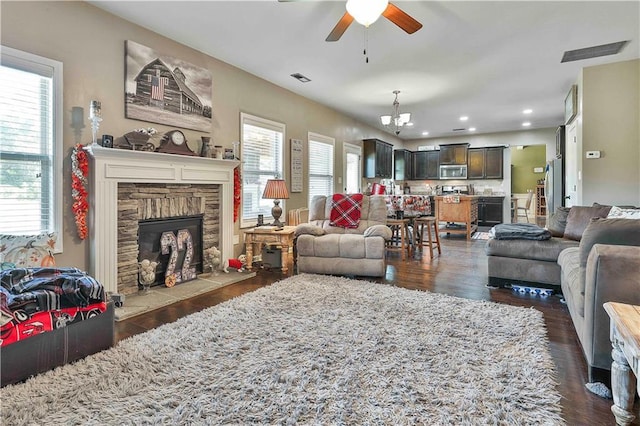 living room with a stone fireplace, a wealth of natural light, dark hardwood / wood-style floors, and ceiling fan with notable chandelier