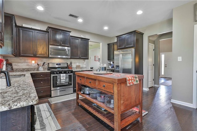 kitchen with dark hardwood / wood-style floors, a center island, backsplash, and appliances with stainless steel finishes