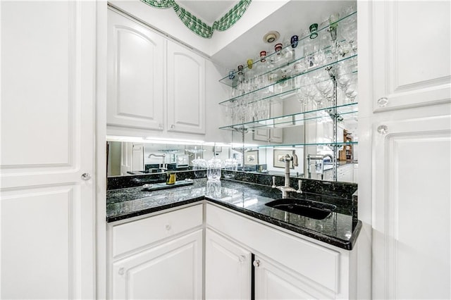 bar with sink, dark stone counters, and white cabinets