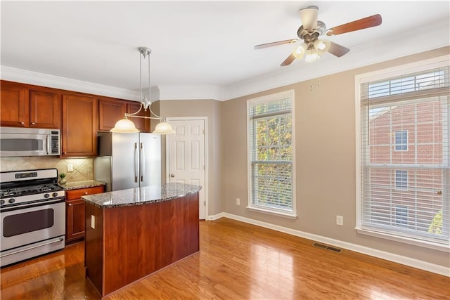 kitchen with hanging light fixtures, appliances with stainless steel finishes, a kitchen island, hardwood / wood-style floors, and backsplash