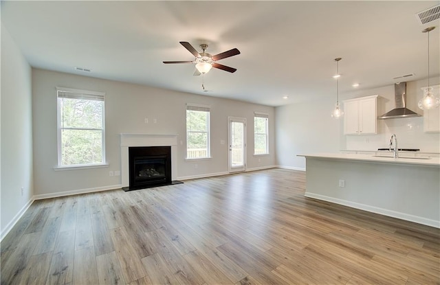 unfurnished living room with a sink, visible vents, light wood-style floors, and a healthy amount of sunlight