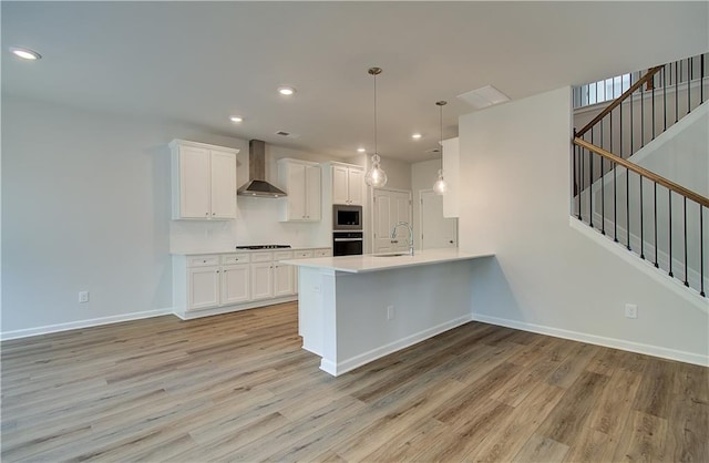 kitchen with a sink, wall chimney range hood, stainless steel microwave, and light wood-style floors