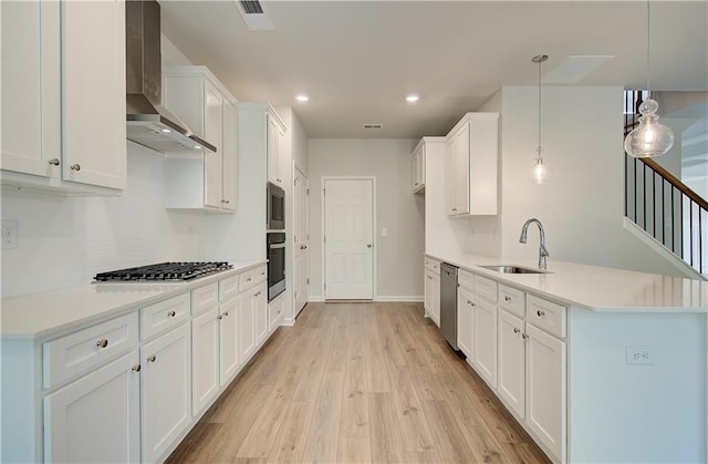 kitchen with visible vents, white cabinets, a sink, wall chimney range hood, and appliances with stainless steel finishes