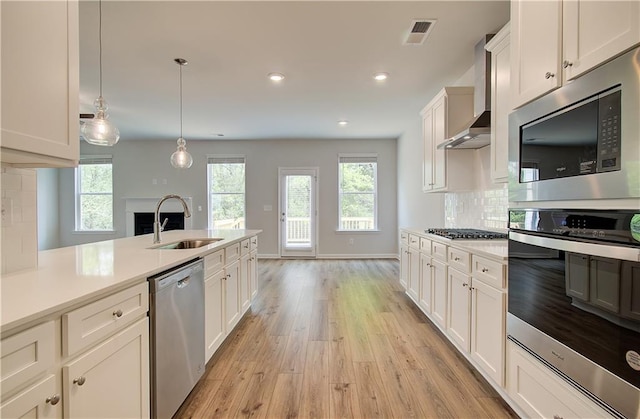 kitchen featuring wall chimney exhaust hood, light wood-style flooring, a sink, light countertops, and stainless steel appliances