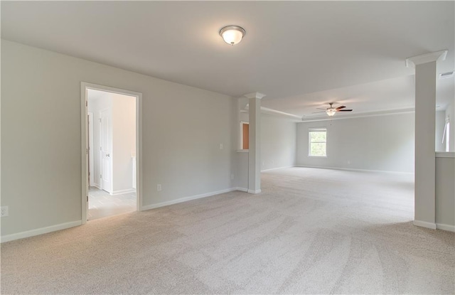 empty room featuring decorative columns, light carpet, baseboards, and ceiling fan