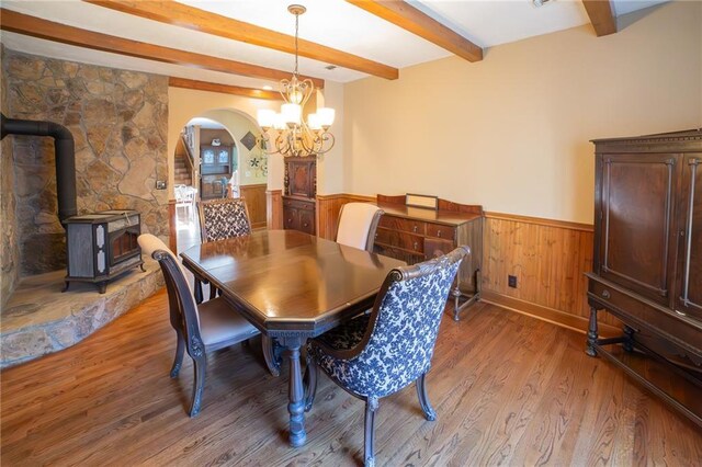 dining area featuring beamed ceiling, hardwood / wood-style flooring, a wood stove, and a chandelier