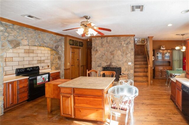 kitchen with ornamental molding, ceiling fan with notable chandelier, black appliances, hardwood / wood-style flooring, and a kitchen island