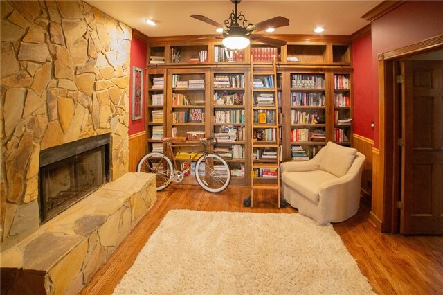 sitting room featuring ceiling fan, a stone fireplace, ornamental molding, and light hardwood / wood-style flooring