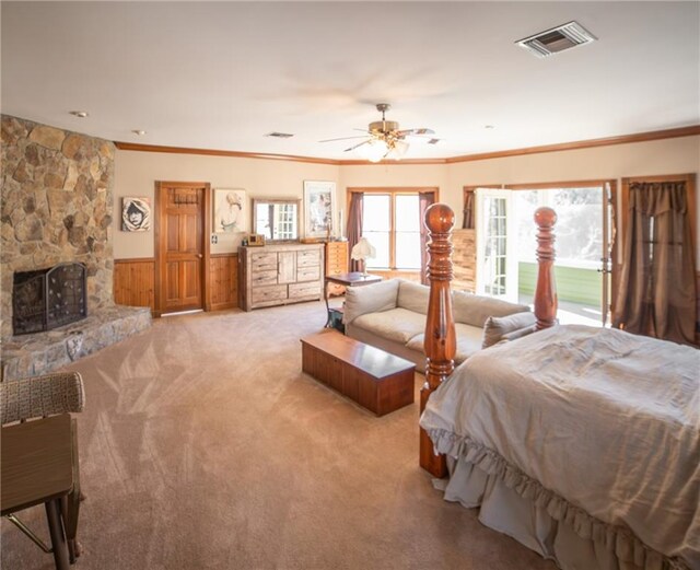 carpeted bedroom with multiple windows, a stone fireplace, ceiling fan, and wooden walls