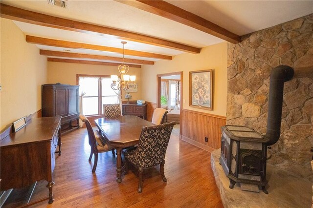 dining space with beam ceiling, an inviting chandelier, a wood stove, and wood-type flooring