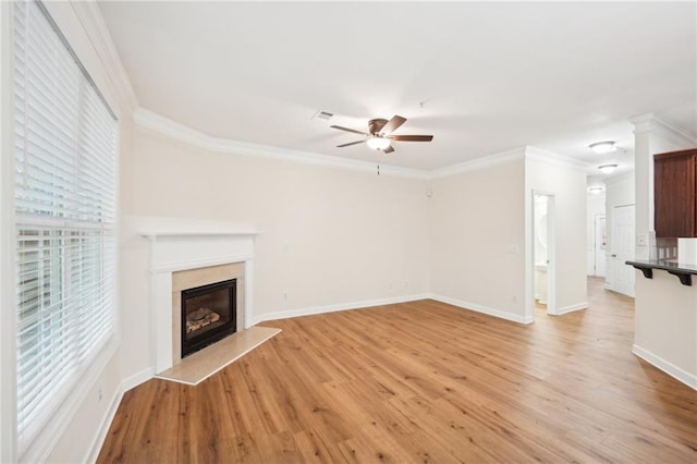 unfurnished living room with ornate columns, light wood-type flooring, ceiling fan, ornamental molding, and a premium fireplace