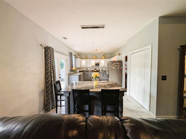 640 Dahoma Trl, Woodstock, GA 30188 - kitchen with stainless steel appliances, white cabinetry, light stone countertops, a breakfast bar, and a textured ceiling