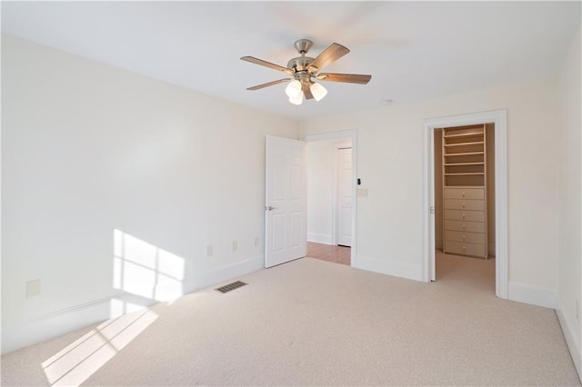 unfurnished bedroom with a closet, a walk in closet, ceiling fan, and light colored carpet