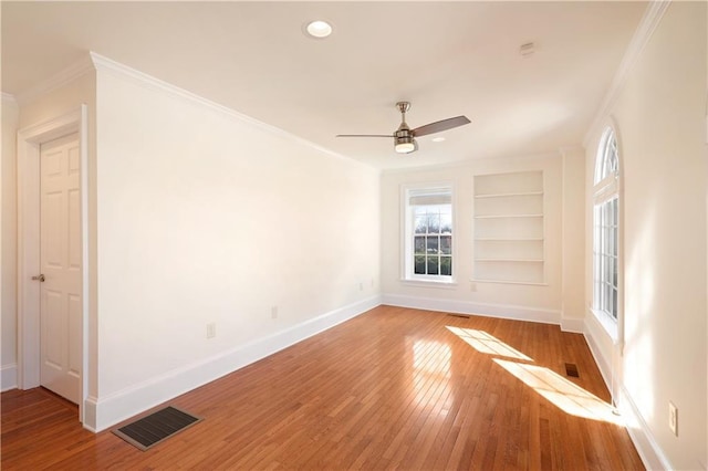 spare room featuring crown molding, built in features, ceiling fan, and light hardwood / wood-style flooring