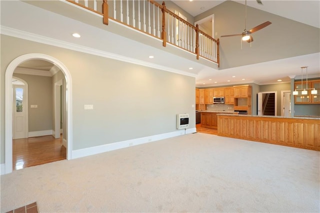 unfurnished living room with crown molding, high vaulted ceiling, light colored carpet, and ceiling fan