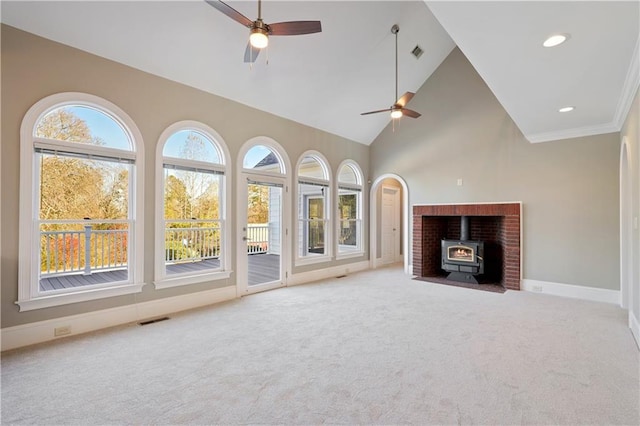 unfurnished living room featuring a wood stove, ceiling fan, light colored carpet, high vaulted ceiling, and crown molding