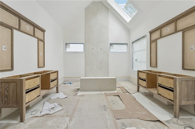 bathroom featuring a skylight, a bathing tub, baseboards, vanity, and high vaulted ceiling