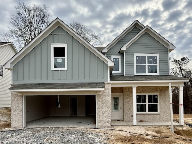 view of front of house featuring a garage, brick siding, board and batten siding, and roof with shingles