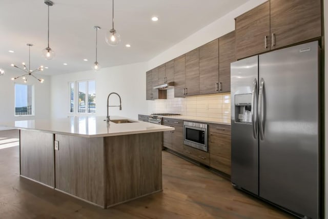 kitchen with backsplash, a kitchen island with sink, sink, dark hardwood / wood-style floors, and stainless steel appliances