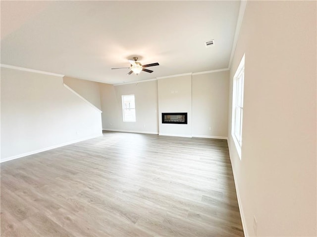 unfurnished living room with ceiling fan, wood finished floors, a glass covered fireplace, and ornamental molding