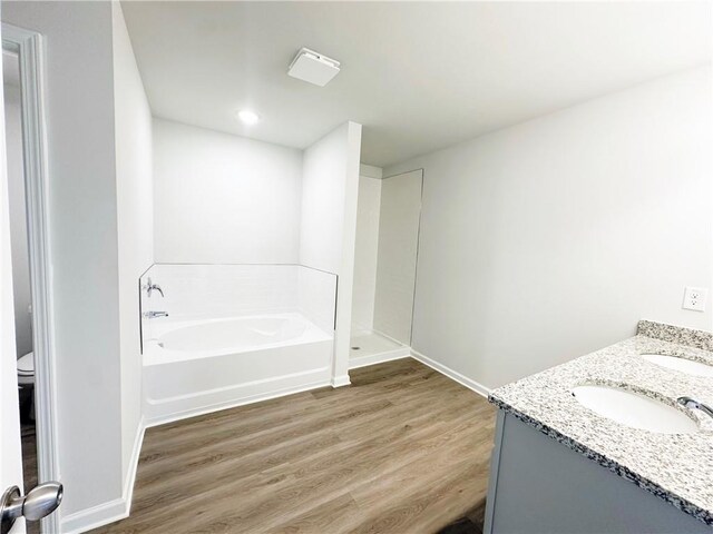 bathroom with a garden tub, toilet, a sink, wood finished floors, and baseboards