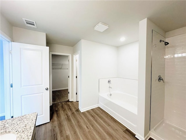 full bath featuring wood finished floors, visible vents, a stall shower, a spacious closet, and a bath