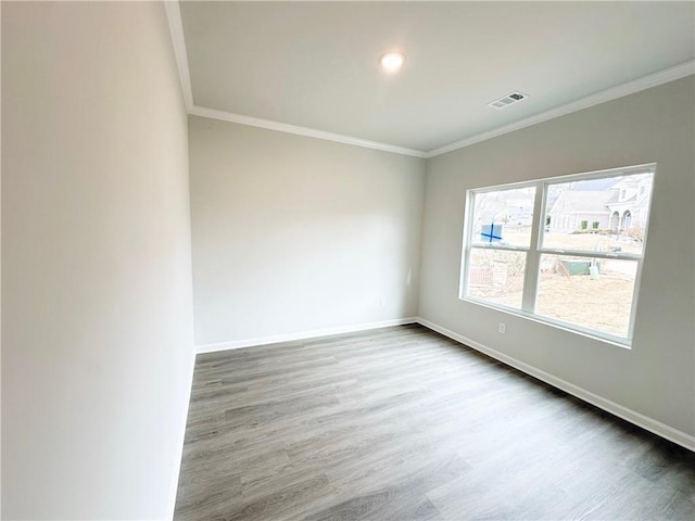 spare room with crown molding, wood finished floors, visible vents, and baseboards