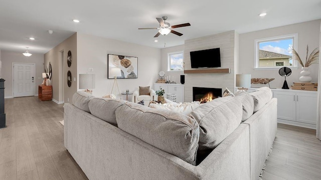 living room with light wood-type flooring, a large fireplace, a ceiling fan, and recessed lighting