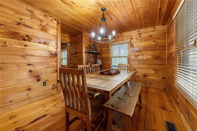 dining space featuring hardwood / wood-style floors, visible vents, an inviting chandelier, wood walls, and wooden ceiling