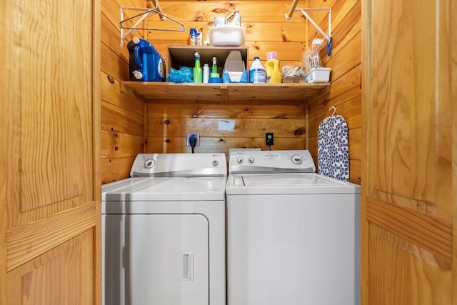 clothes washing area featuring separate washer and dryer and wood walls