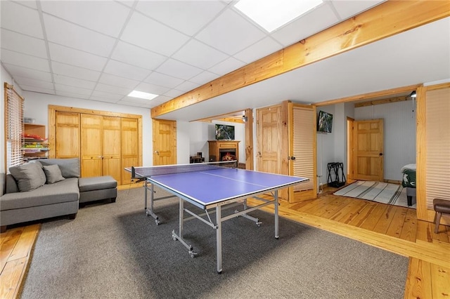 playroom featuring a drop ceiling, wood finished floors, and a warm lit fireplace