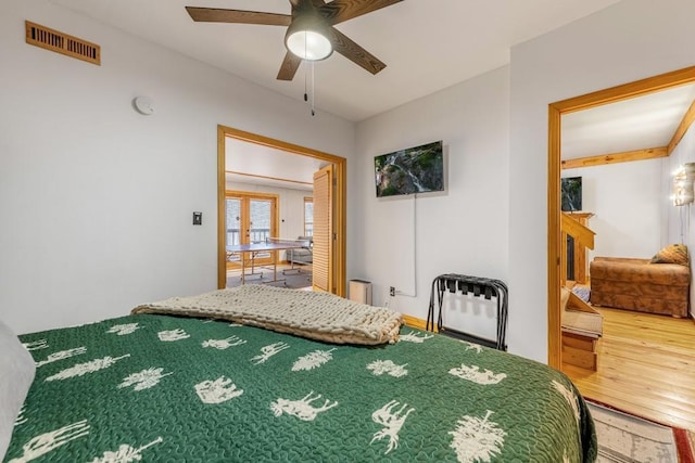 bedroom with hardwood / wood-style flooring, a fireplace, french doors, and ceiling fan