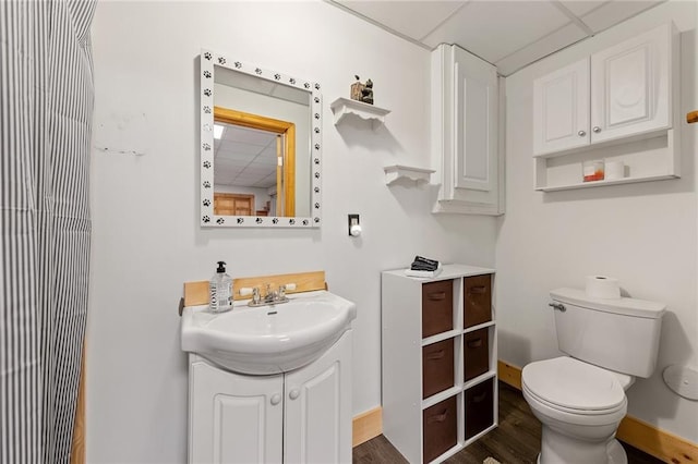 bathroom with toilet, a drop ceiling, wood finished floors, baseboards, and vanity