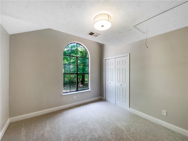 unfurnished bedroom with a textured ceiling, light colored carpet, a closet, and lofted ceiling