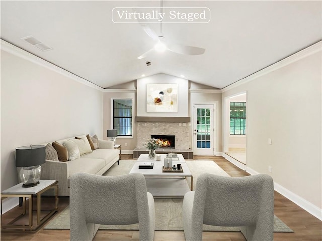 living room with vaulted ceiling, ceiling fan, ornamental molding, wood-type flooring, and a stone fireplace