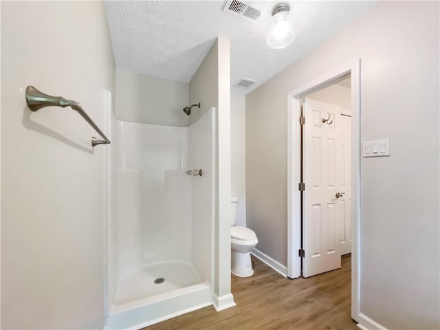 bathroom featuring toilet, a textured ceiling, wood-type flooring, and walk in shower